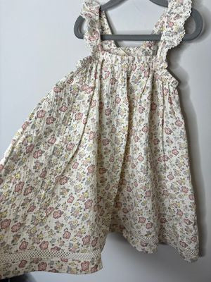 Cream floral dress with ruffle straps and lace trim, featuring pink and yellow flowers, hanging on a hanger.