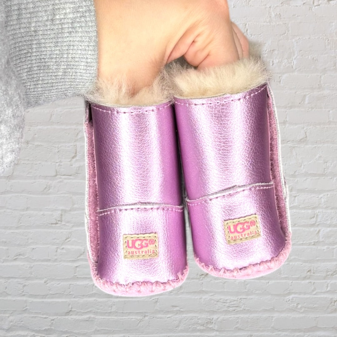 Pair of metallic pink baby booties with soft faux fur lining, held by a hand.