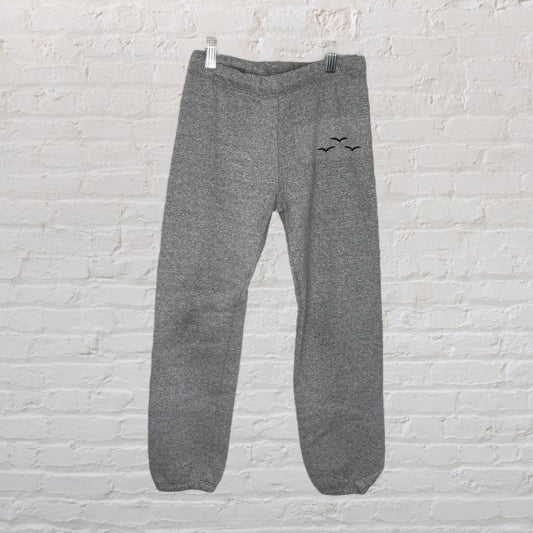 Grey unisex sweatpants featuring subtle bird embroidery, displayed against a white brick wall.