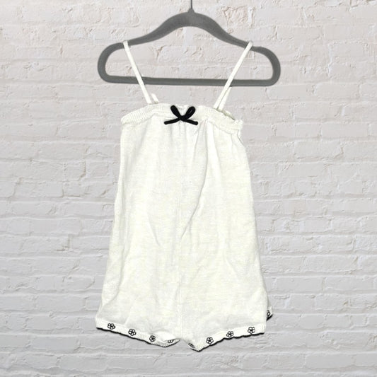 White spaghetti strap playsuit with a black bow accent and floral hem, hanging on a gray hanger.