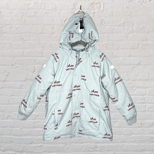 Light blue hooded jacket with 'shoo worries' print in maroon, displayed on a hanger against a brick wall.