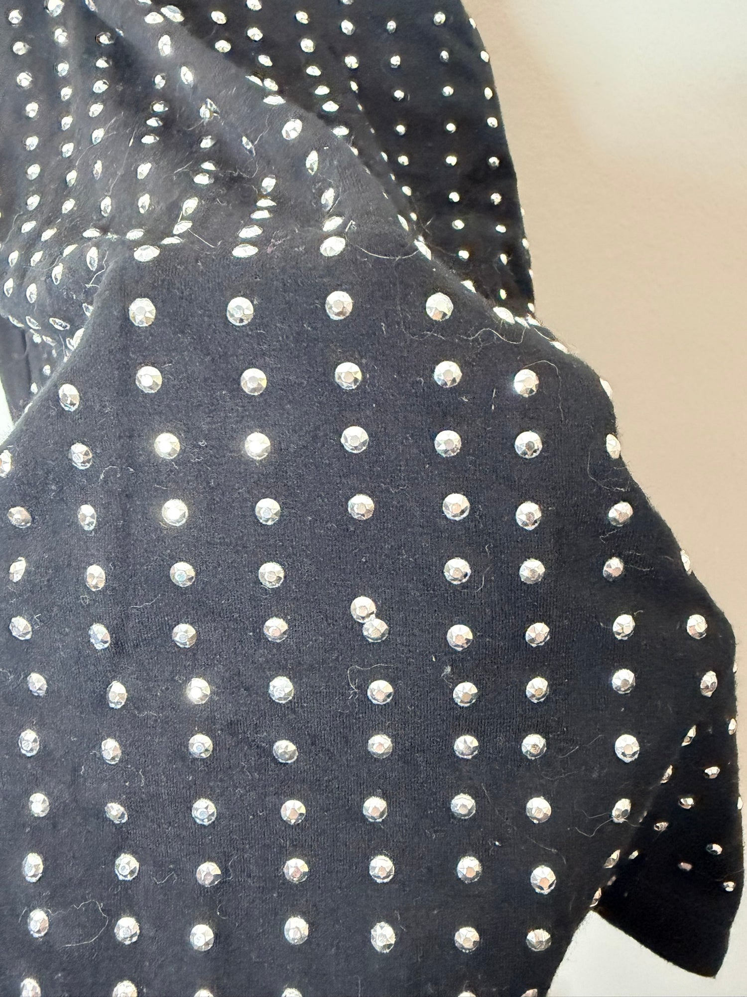 Black sleeveless dress with silver studs, hanging on a hanger against a white brick wall.