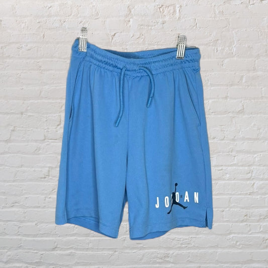 Blue Jordan athletic shorts with drawstring waist and logo near the hem, displayed against a brick wall background.