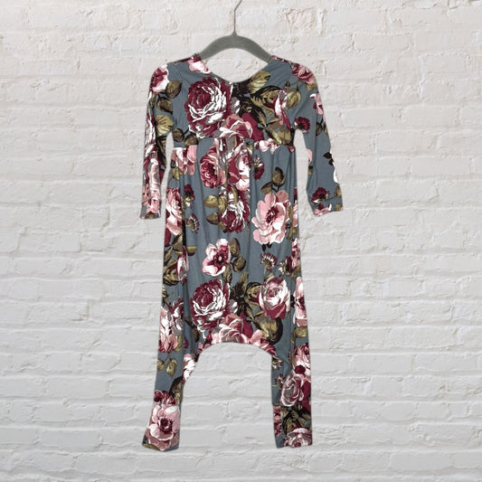 Baby romper with blue and burgundy floral pattern hanging on a hanger against a brick wall.
