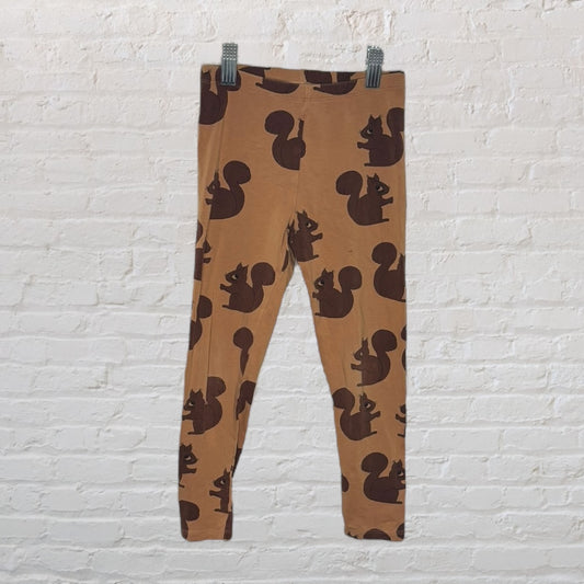 Brown leggings with a dark brown squirrel print pattern, hanging against a white brick wall.