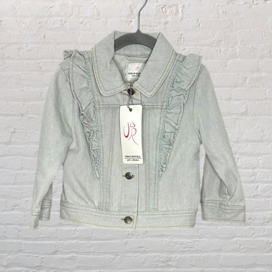 Urban Republic girls' denim jacket with ruffle detailing, hanging on a black hanger against a white brick background.