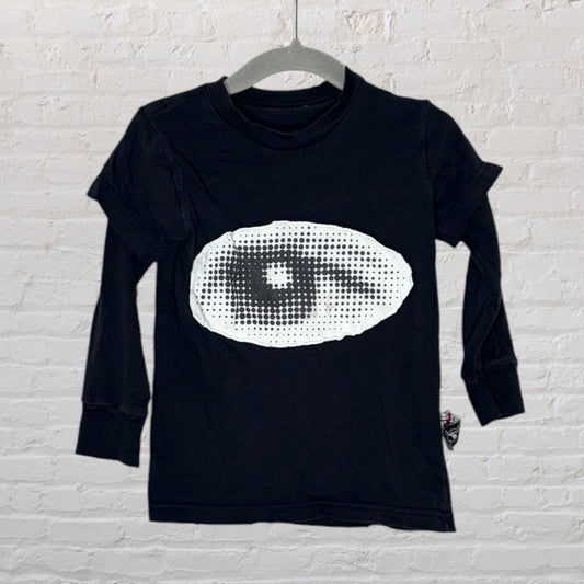 Black long sleeve t-shirt with a large white graphic eye design on the front, hanging against a brick wall backdrop.