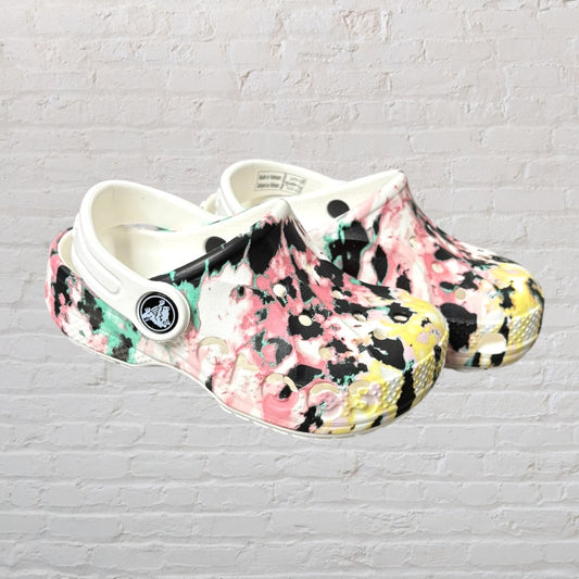 Pair of Crocs with a multicolor tie-dye pattern, featuring a flexible strap and ventilation holes.