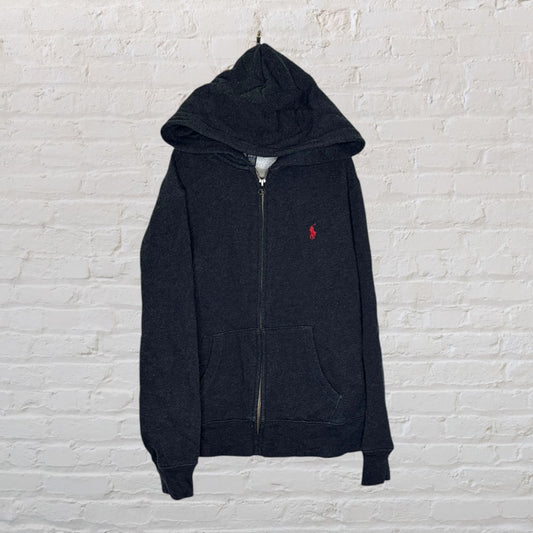 Charcoal zip-up hoodie by Ralph Lauren with a red polo logo, hanging against a white brick wall.
