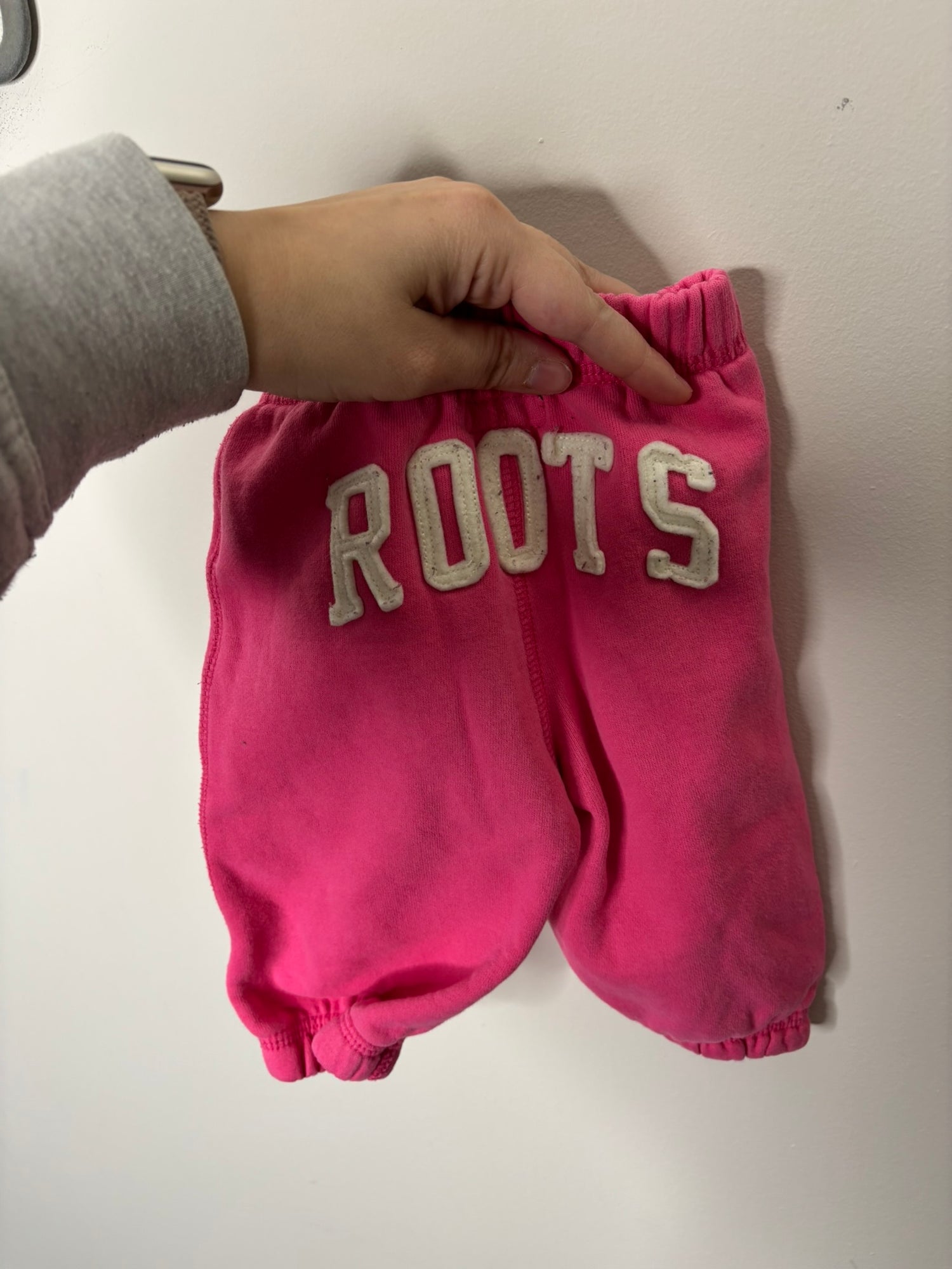 Pink Roots zip-up hoodie set with logo, featuring a hood and front pockets, displayed on a hanger.