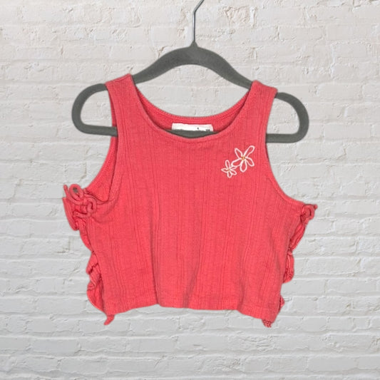 Coral ribbed crop top with side tie details and small flower embroidery on the chest, hanging on a hanger.