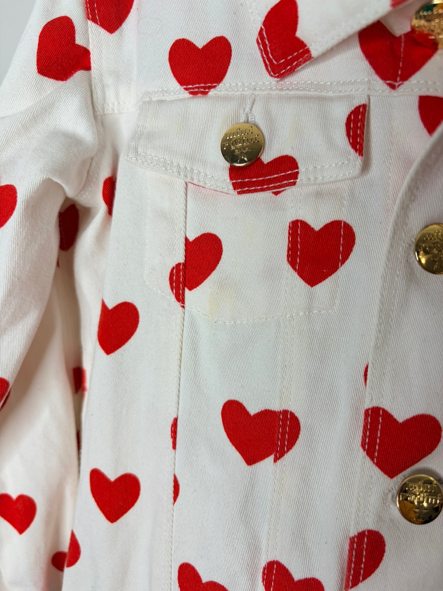 Mini Rodini white denim jacket with red heart prints and gold buttons.