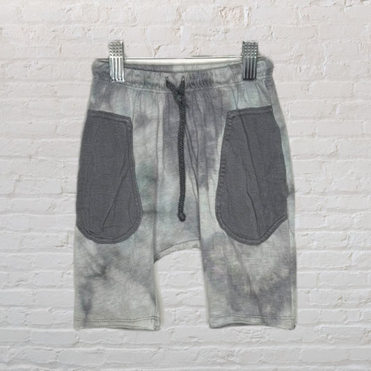 Grey tie-dye shorts with large pockets and a drawstring waistband, hanging on a white textured background.