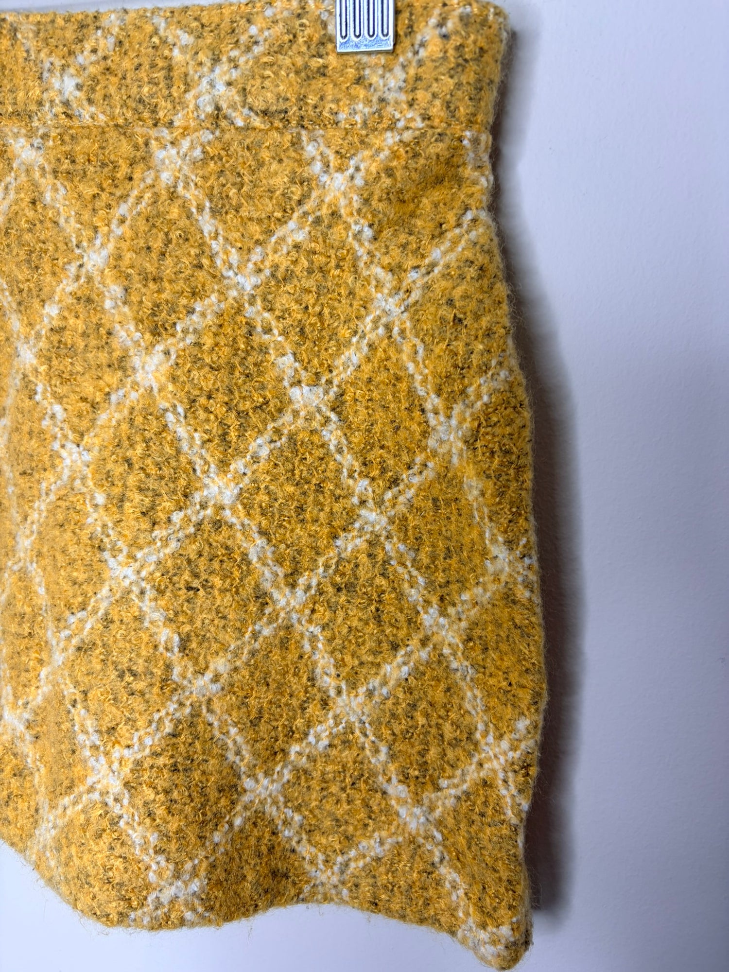 Mustard yellow textured mini skirt with a diamond pattern, clipped on a white brick background.