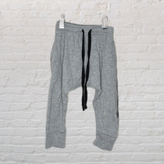 Grey jogger sweatpants with black drawstring hanging against a white brick wall.