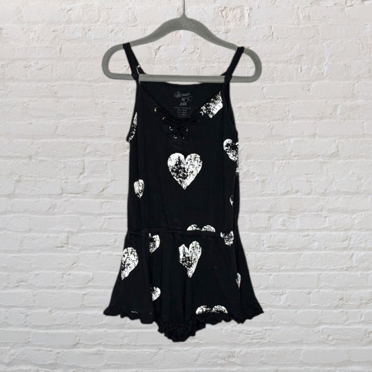 Black romper with silver heart prints and spaghetti straps, featuring a lace-up neckline detail, hanging on a hanger.