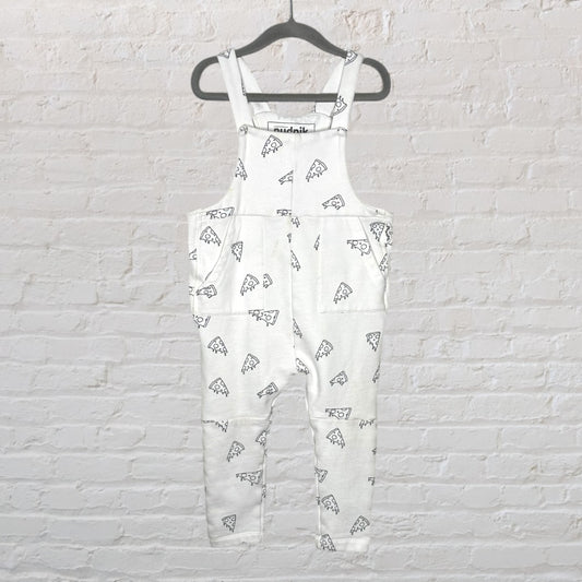 White overalls with black pizza print design, hanging on a dark hanger against a white brick wall.