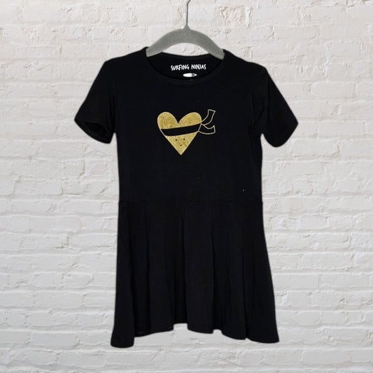 Black dress with gold heart print and short sleeves, labeled Surfing Ninjas, on a hanger against a white brick wall.