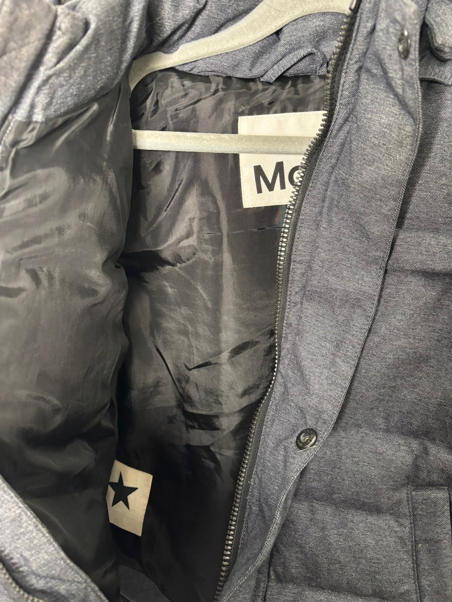 Charcoal grey hooded puffer jacket with button and zipper front, displayed against a white brick wall.