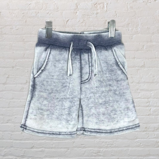 Gray acid wash shorts with a drawstring waist, hanging on a hanger against a brick wall.