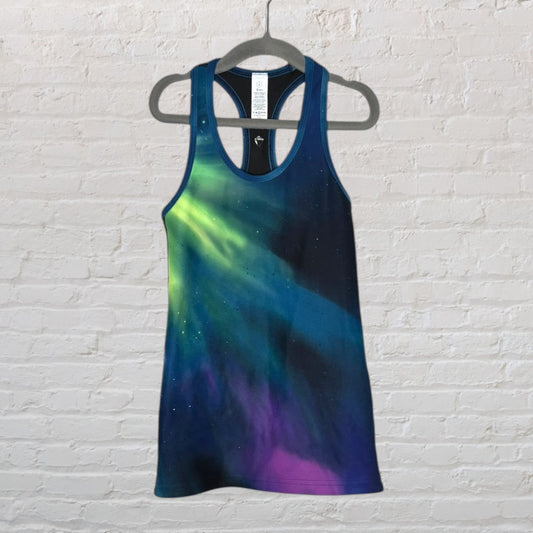 Women's racerback tank top with a galaxy print in shades of blue, green, and purple, hanging on a hanger.