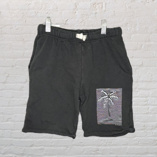 Black shorts with a white palm tree graphic on the leg, displayed against a brick wall.