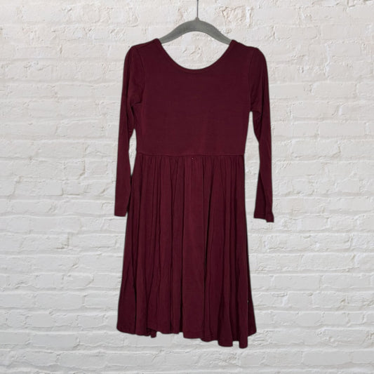 Burgundy long-sleeve midi dress with a fitted top and flowing skirt, hanging on a hanger against a white brick wall.