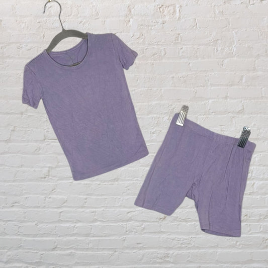 Purple short sleeve pajama set with top and shorts hanging on a white brick wall.