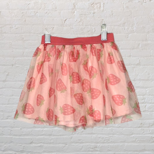 Pink tulle skirt with a strawberry print pattern, hanging on a white brick wall.
