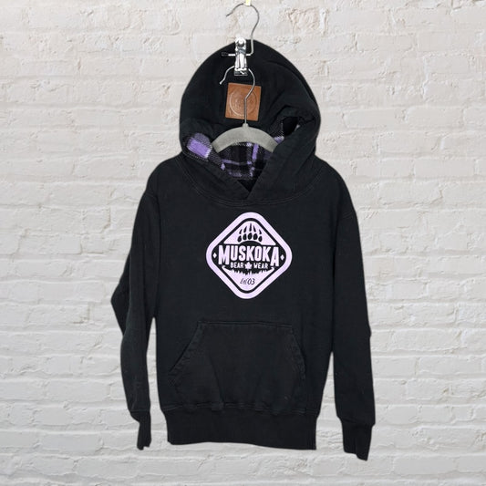Black Muskoka Bear Wear hoodie with purple plaid-lined hood hanging on a hanger.