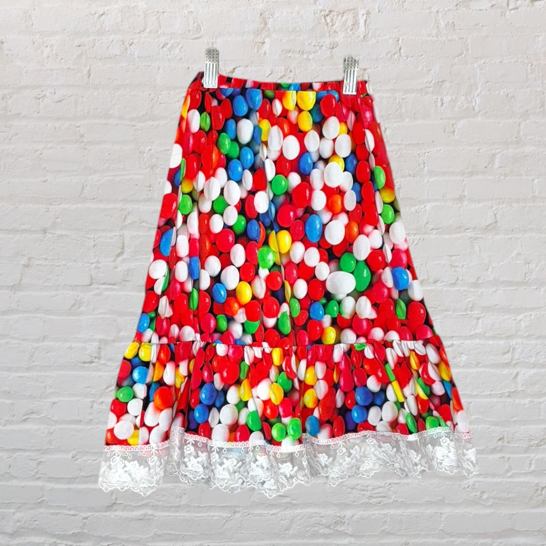A vibrant skirt with a colorful candy print and lace trimming, hanging against a white brick wall.