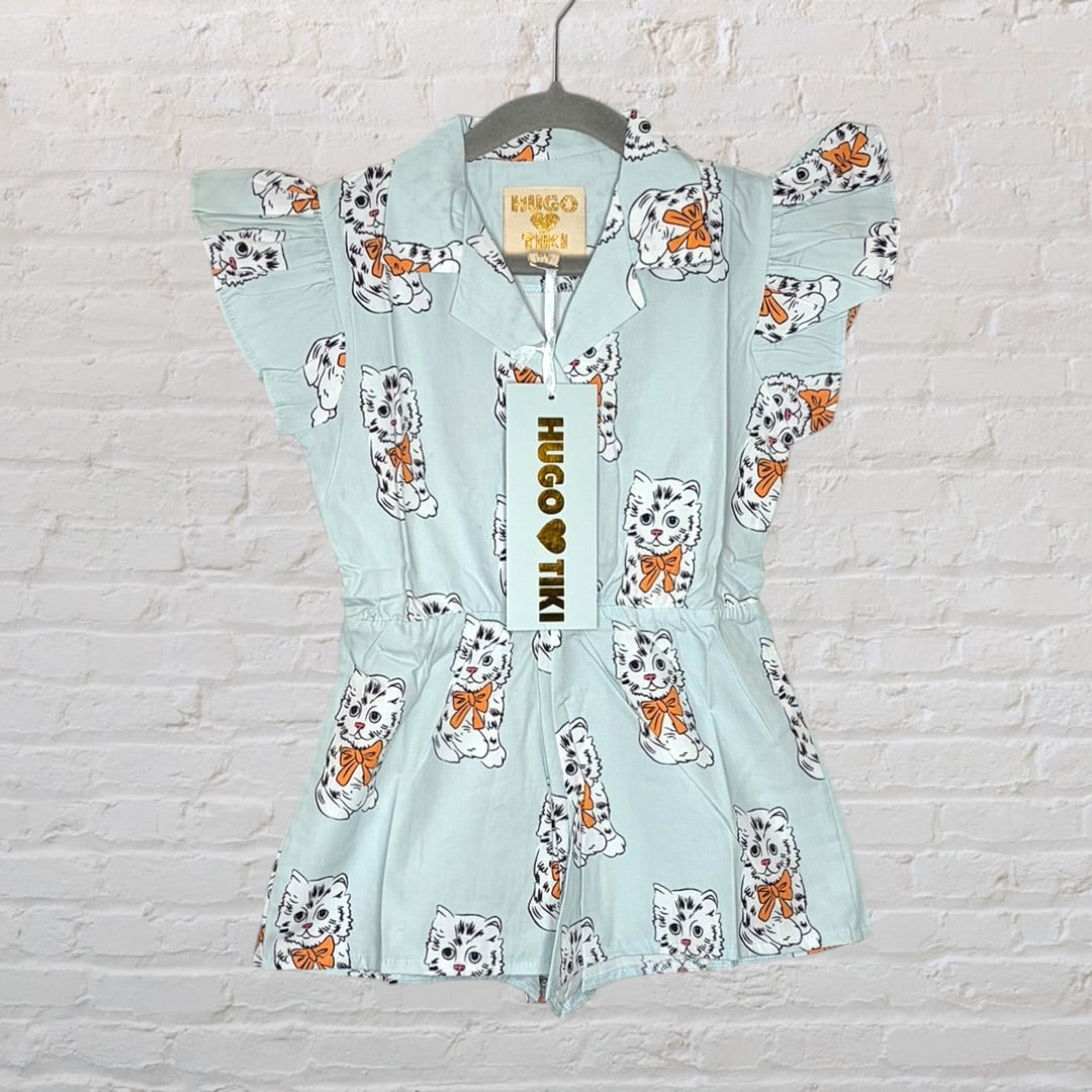 Light blue romper with cat print and ruffle sleeves by Hugo Loves Tiki, hanging on a hanger with a tag attached.