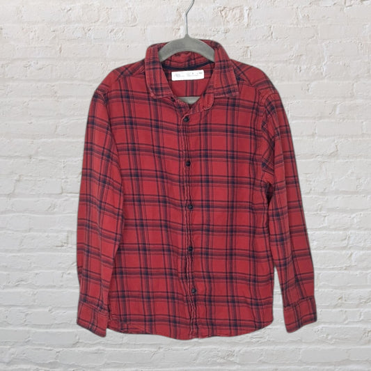 Red and black plaid button-up shirt on a hanger against a white brick wall.