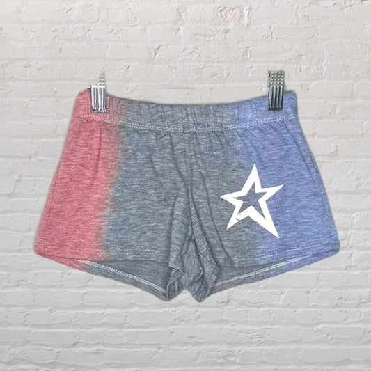Red, grey, and blue tie-dye shorts with white star graphic, hung against a white brick wall.