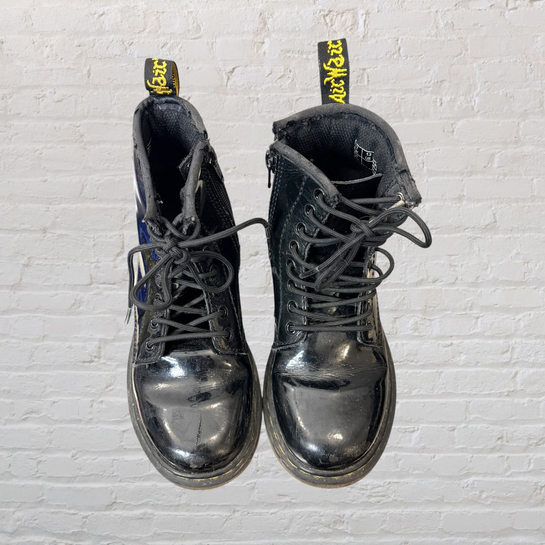 Shiny black patent leather lace-up boots with yellow stitching and pull tabs, showing visible wear.