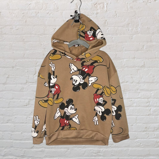 Brown hoodie with an all-over print of Mickey Mouse in various playful poses, displayed against a white brick wall.
