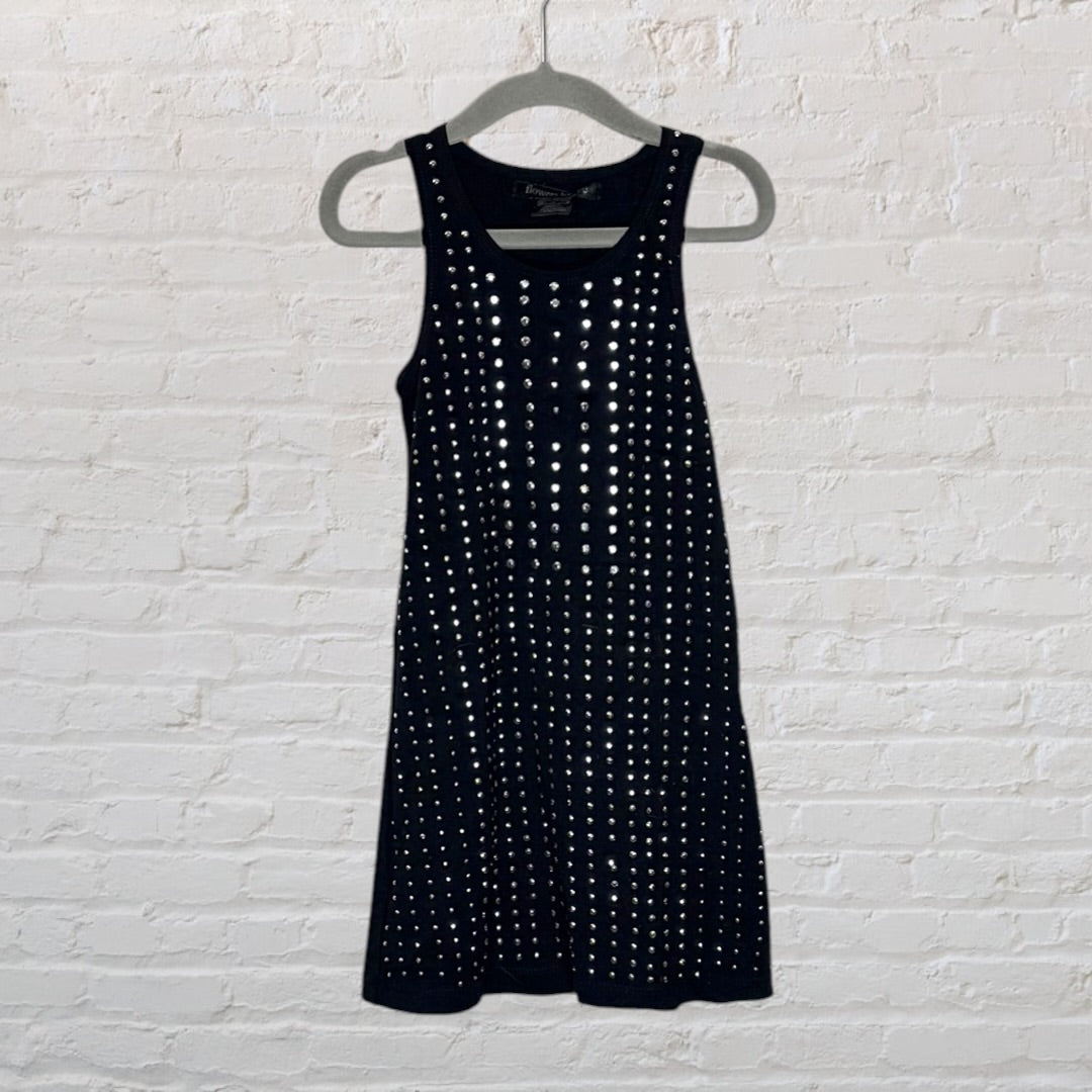 Black sleeveless dress with silver studs, hanging on a hanger against a white brick wall.