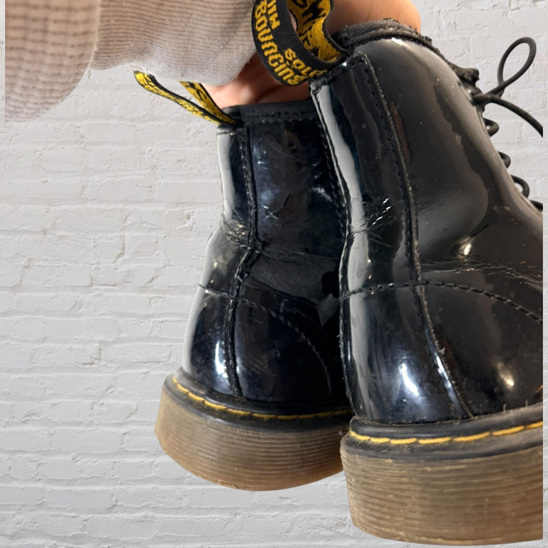 Shiny black patent leather lace-up boots with yellow stitching and pull tabs, showing visible wear.
