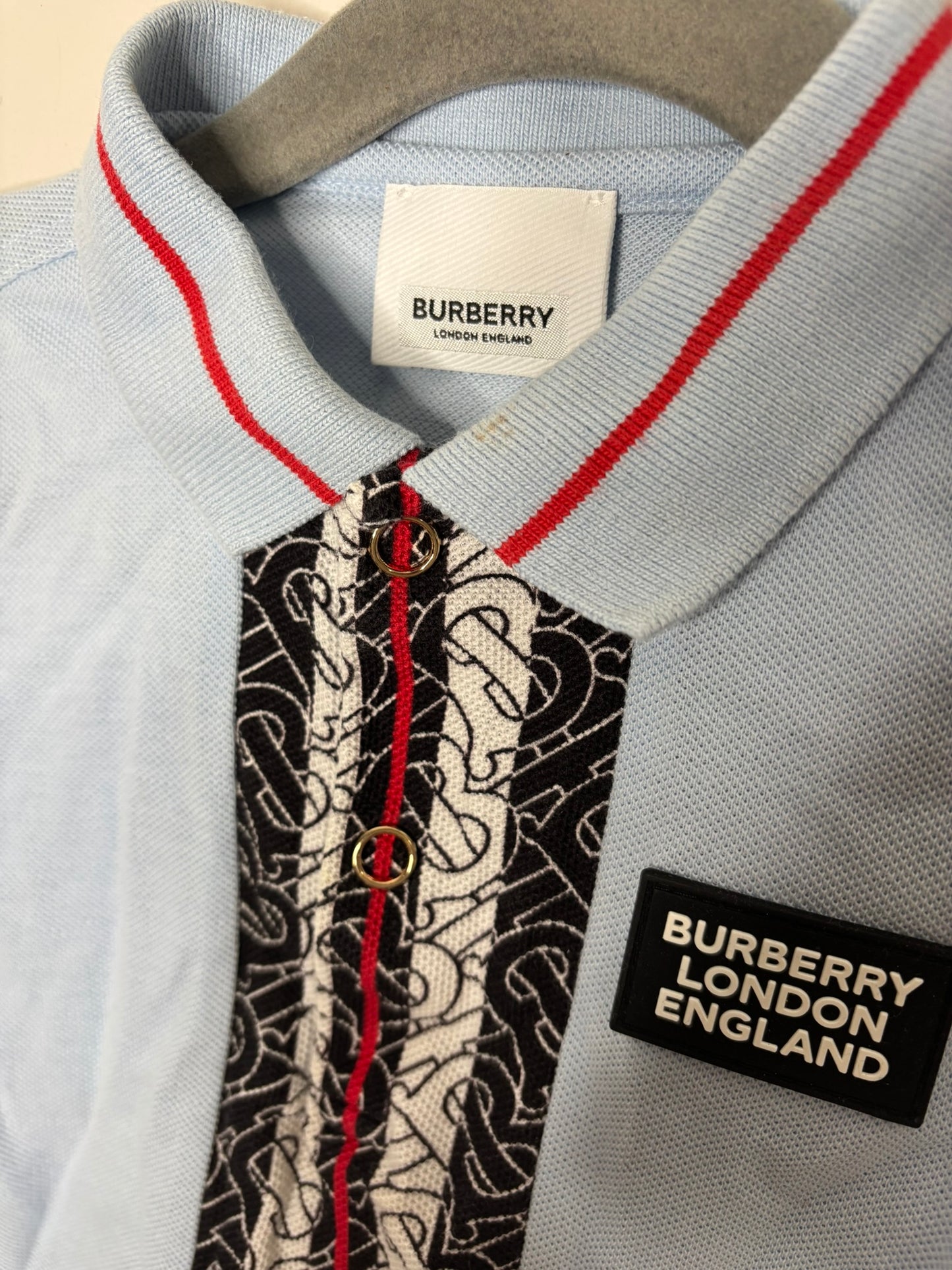 Light blue Burberry London polo shirt with black and white pattern strip and brand logo on the front.