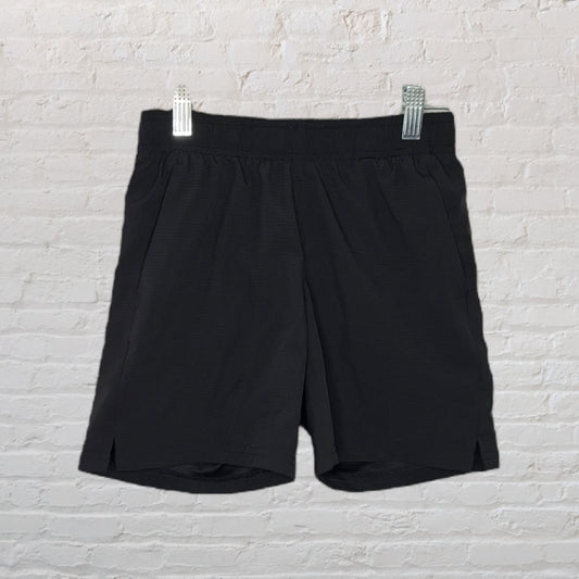 A pair of men's black athletic shorts hanging against a white brick wall.