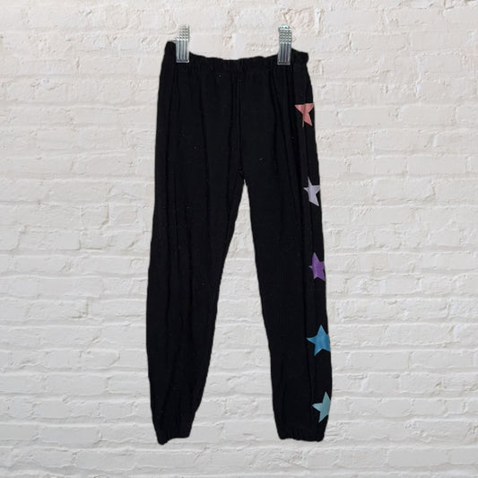 Black leggings with multicolored stars on the side, hanging on clips against a white brick wall.
