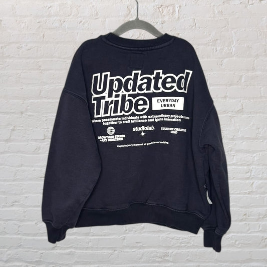Black sweatshirt with 'Updated Tribe' graphic print on the back, hanging against a brick wall.