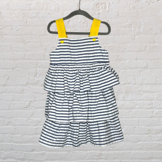 Black and white striped tiered dress with yellow straps and heart-shaped buttons, hanging on a hanger.