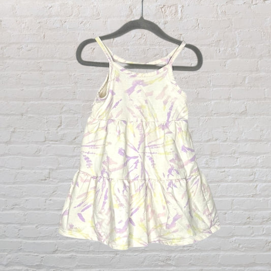 White sundress with pastel lavender and yellow tie-dye pattern, featuring spaghetti straps, displayed on a hanger.