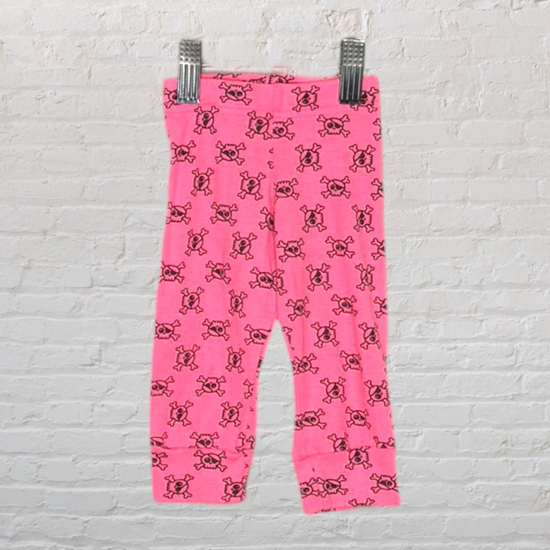 Bright pink leggings with a repeating black skull pattern, displayed on a hanger against a brick wall.