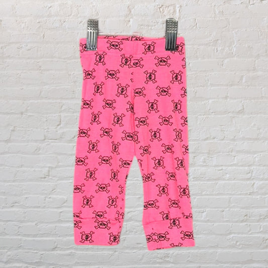 Bright pink leggings with a repeating black skull pattern, displayed on a hanger against a brick wall.