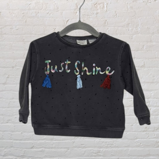 Black polka dot sweatshirt with 'Just Shine' text and colorful tassels, displayed on a hanger.