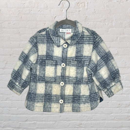 Blue and white plaid shacket with button closure, displayed on a hanger against a white brick wall.