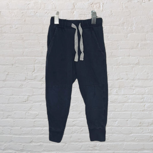 Navy blue jogger sweatpants with grey drawstring, displayed against a brick wall.