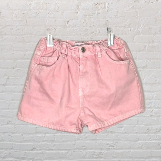 Light pink vintage high-waisted shorts with pockets, displayed against a brick wall background.